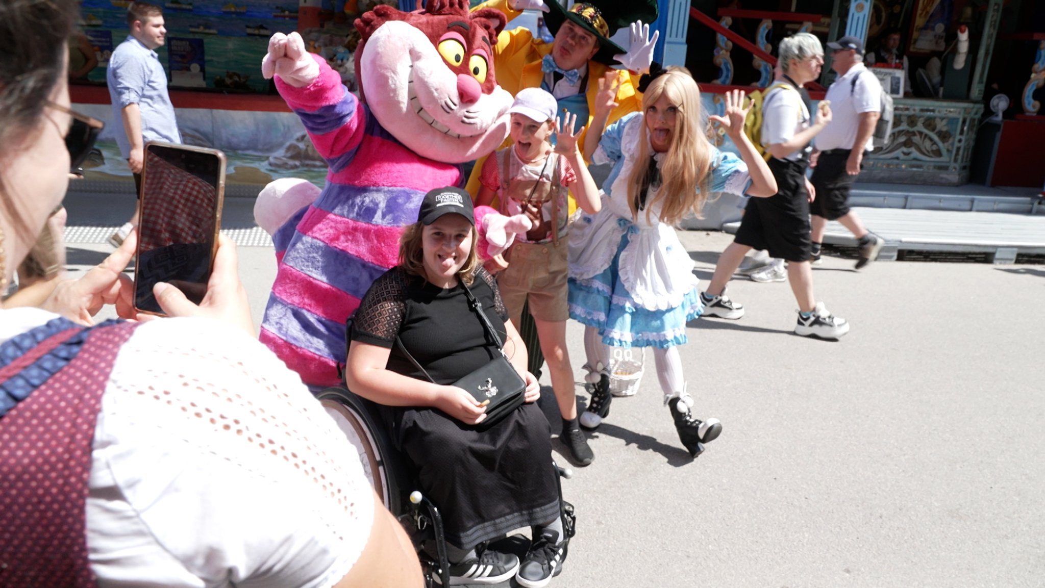 Ein Mädchen im Rollstuhl und ihre Schwester machen ein witziges Bild mit drei Schauspielern auf dem Gäubodenvolksfest in Straubing. Die Mutter der Mädchen macht ein Foto davon.