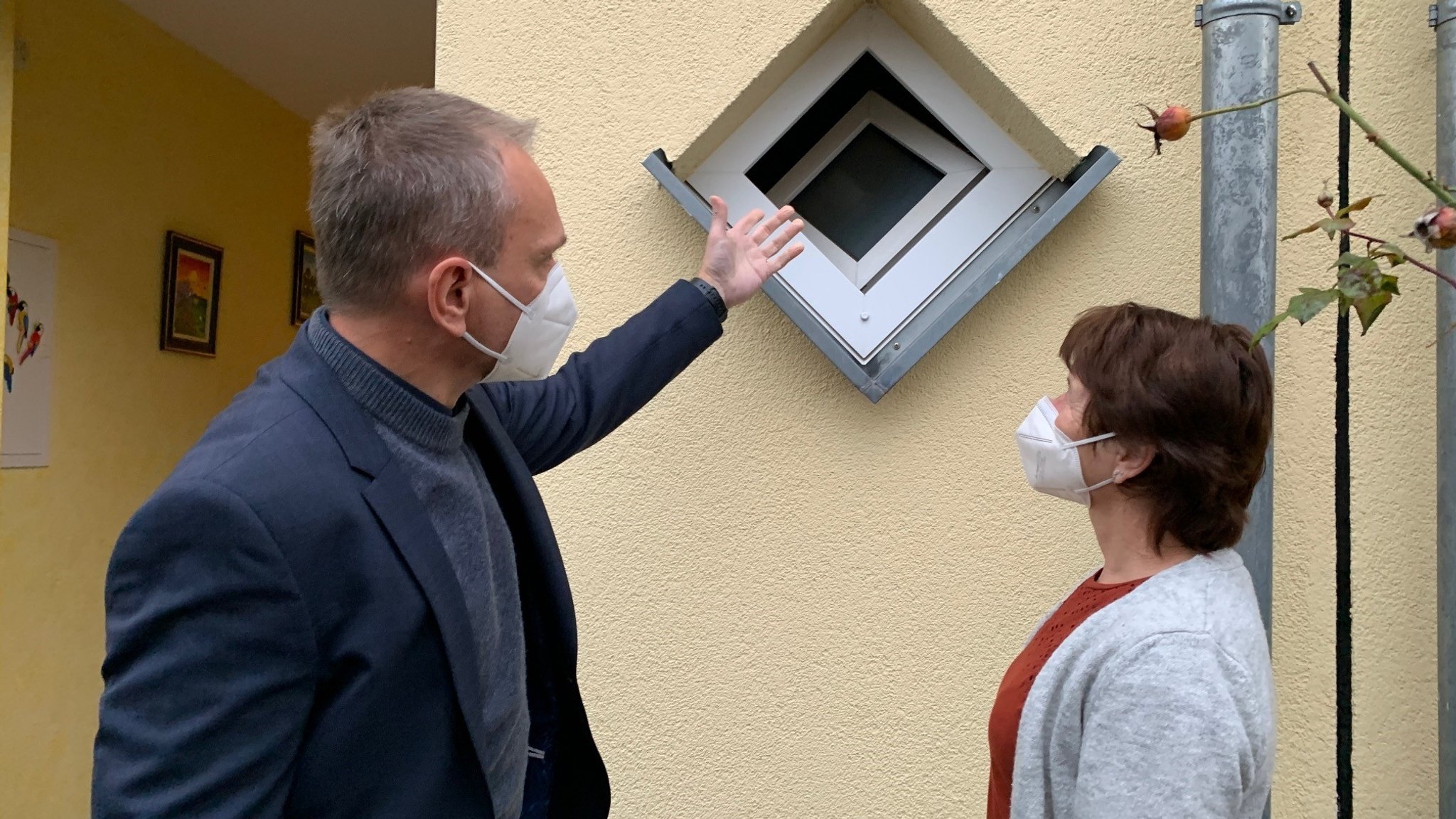 Polizist mit Bewohnerin vor einem kleinen Fenster. 