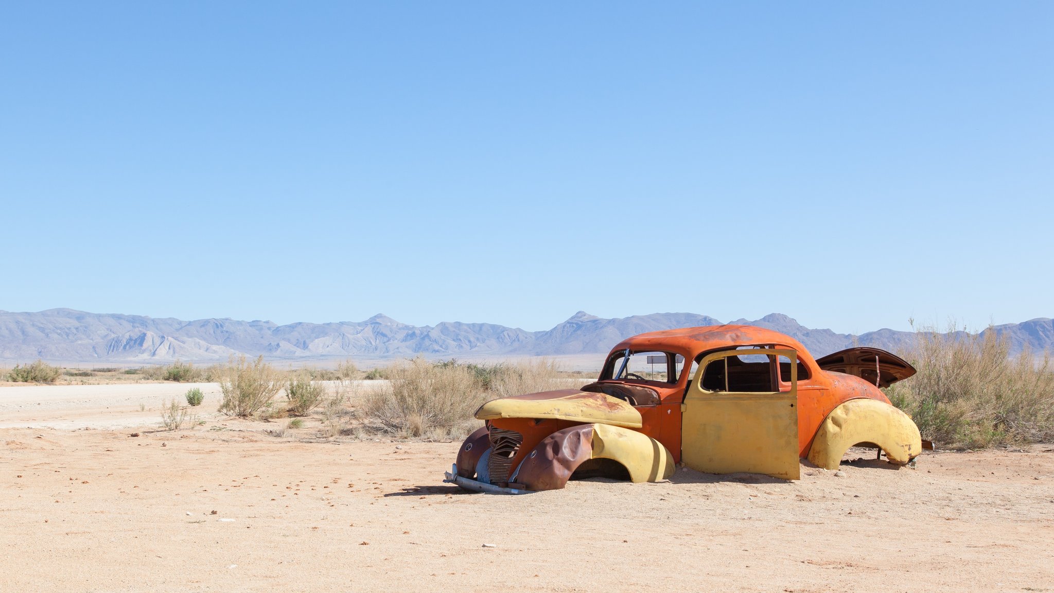 Vor sich hin verrottender VW-Käfer steht mitten in einer Wüstenlandschaft in Afrika.