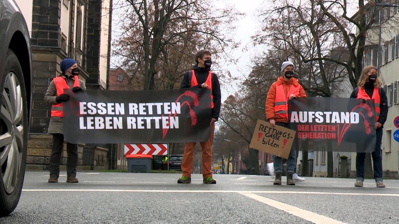 Klimaaktivisten stehen mit Plakaten auf einer Straße.