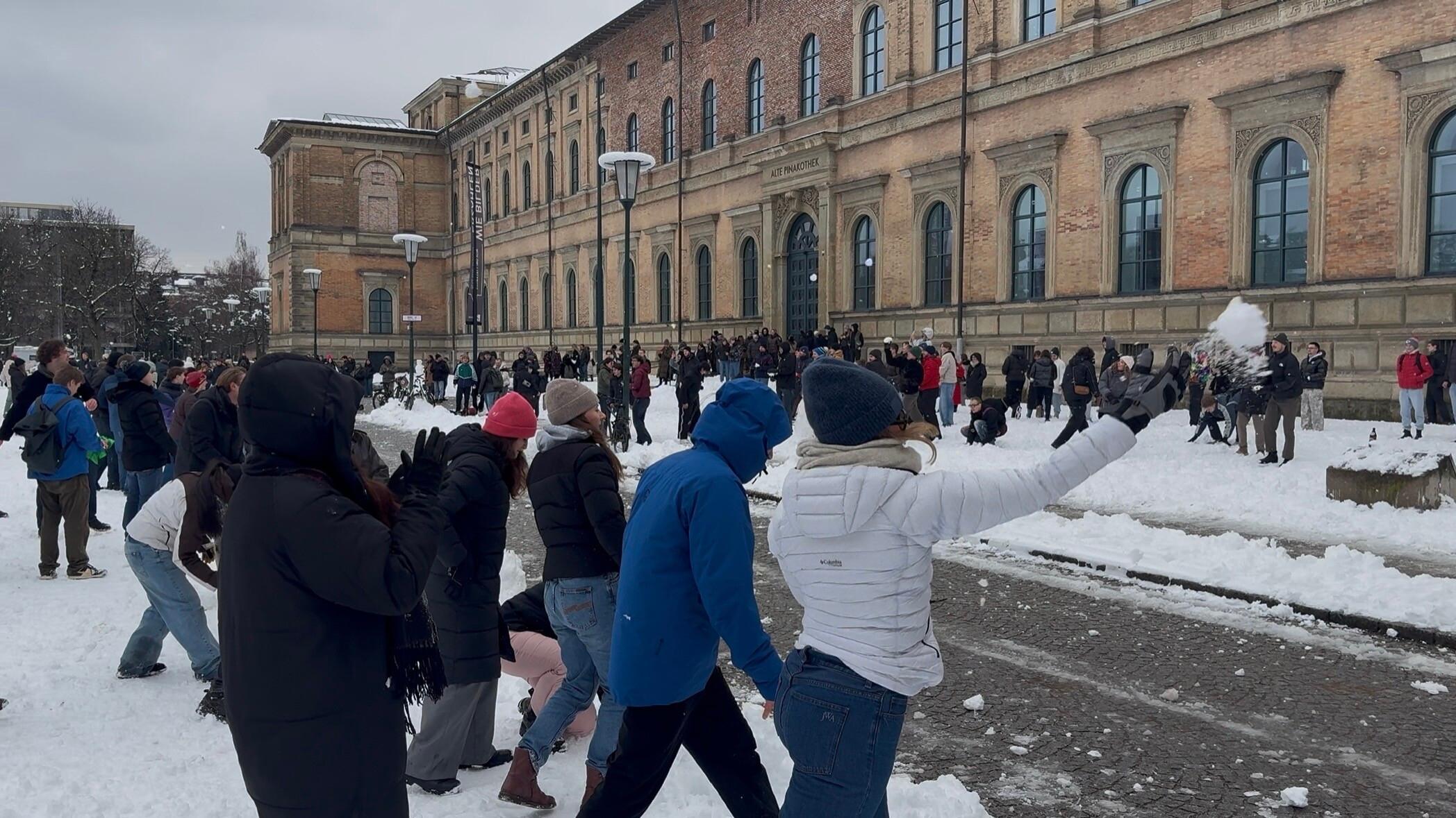 Personen nehmen an einer Schneeballschlacht vor der Alten Pinakothek in München teil. 
