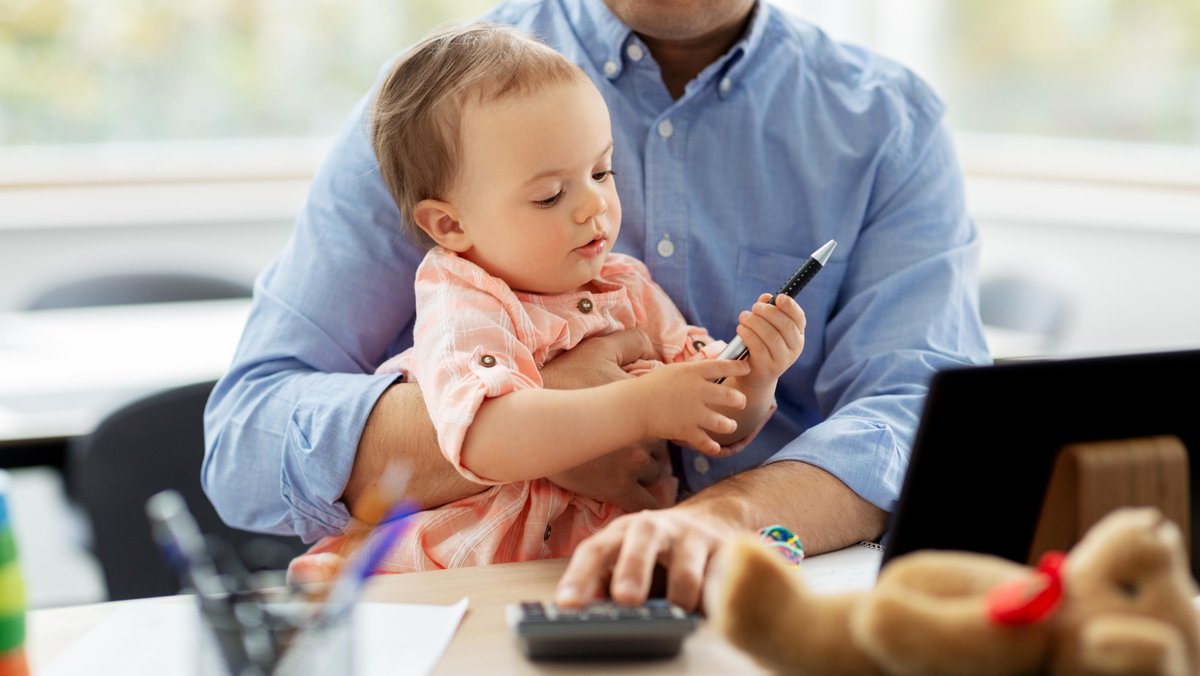 Ein Mann passt auf ein Kind auf und benutzt dabei einen Taschenrechner