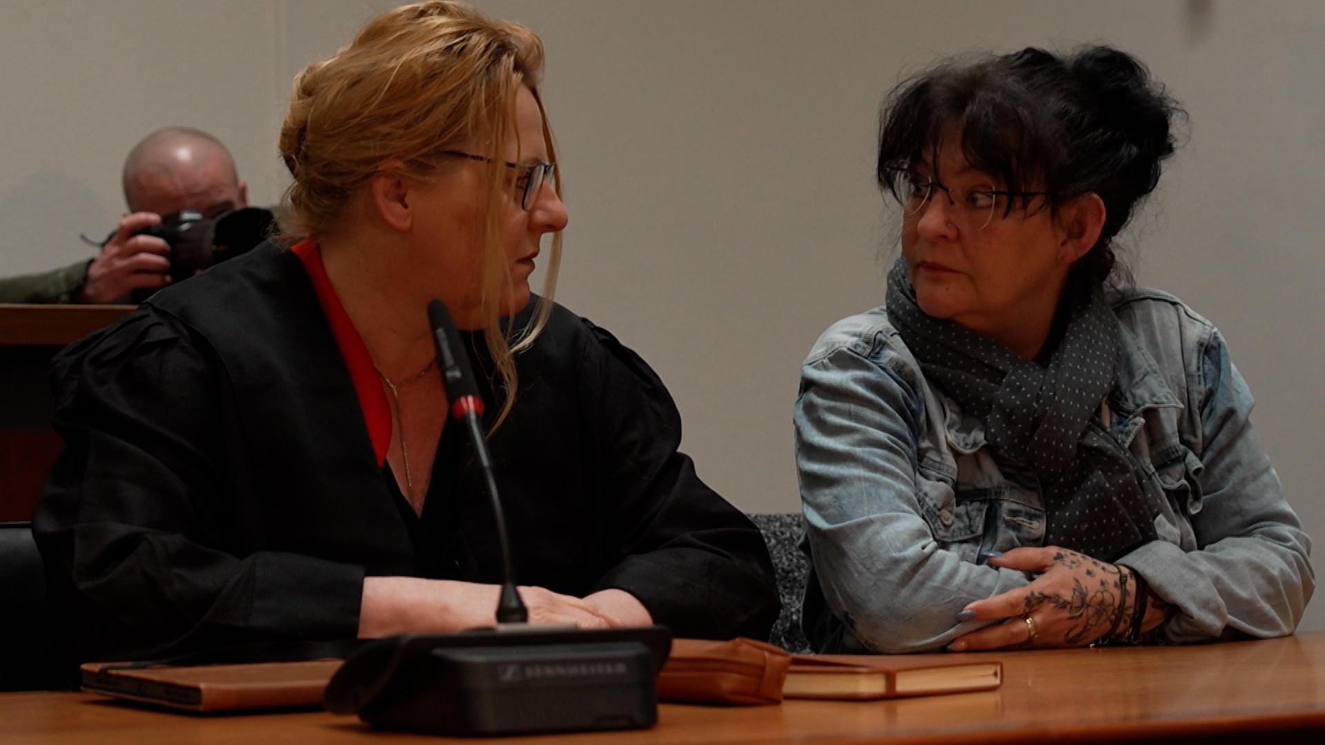 Ein Frau sitzt auf einer Anklagebank, neben ihr eine Anwältin.