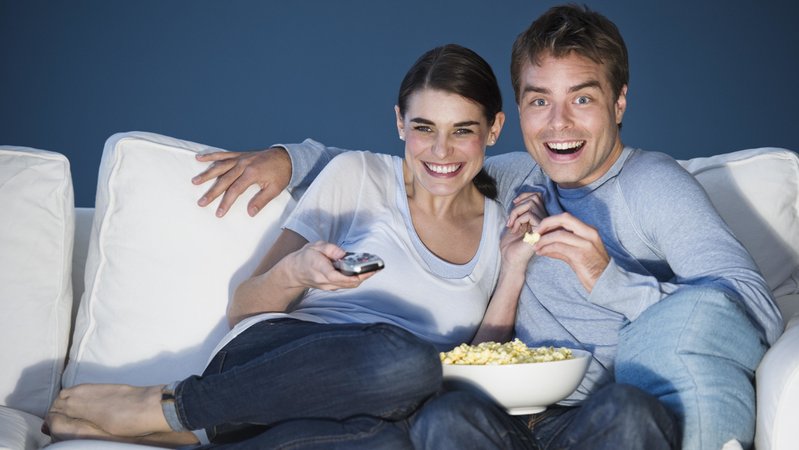 Paar lachend vor dem Fernseher mit Popcorn.