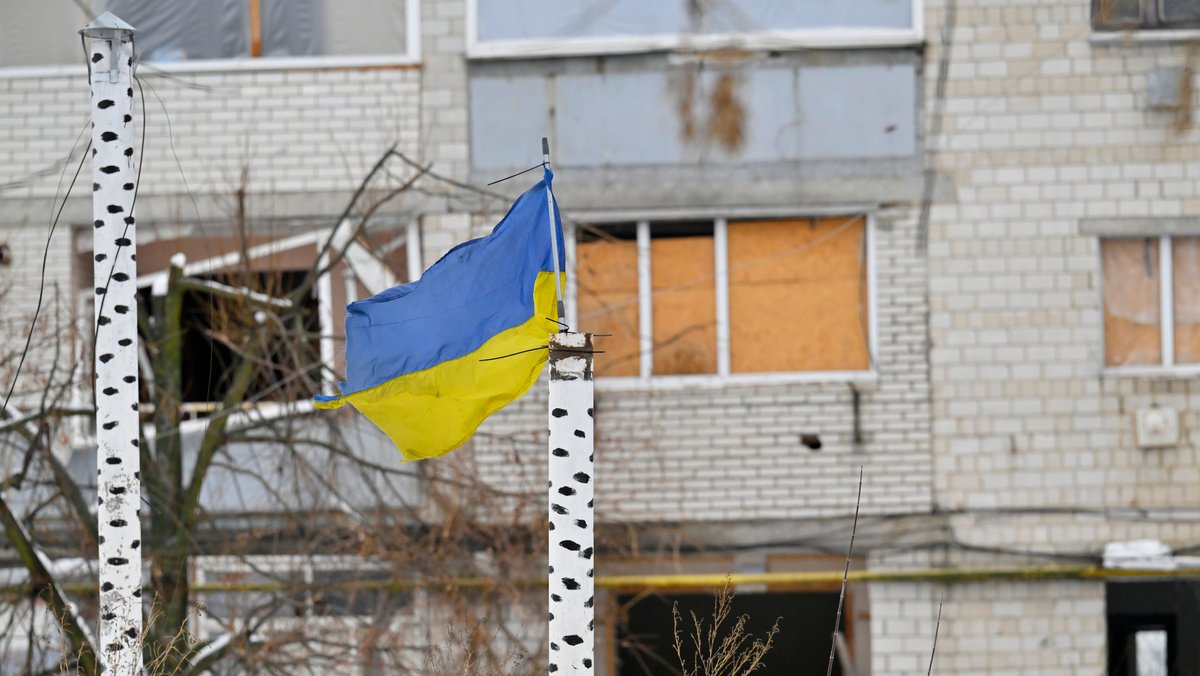 Zerstörtes Haus in der Ukraine. Davor weht die ukrainische Fahne.