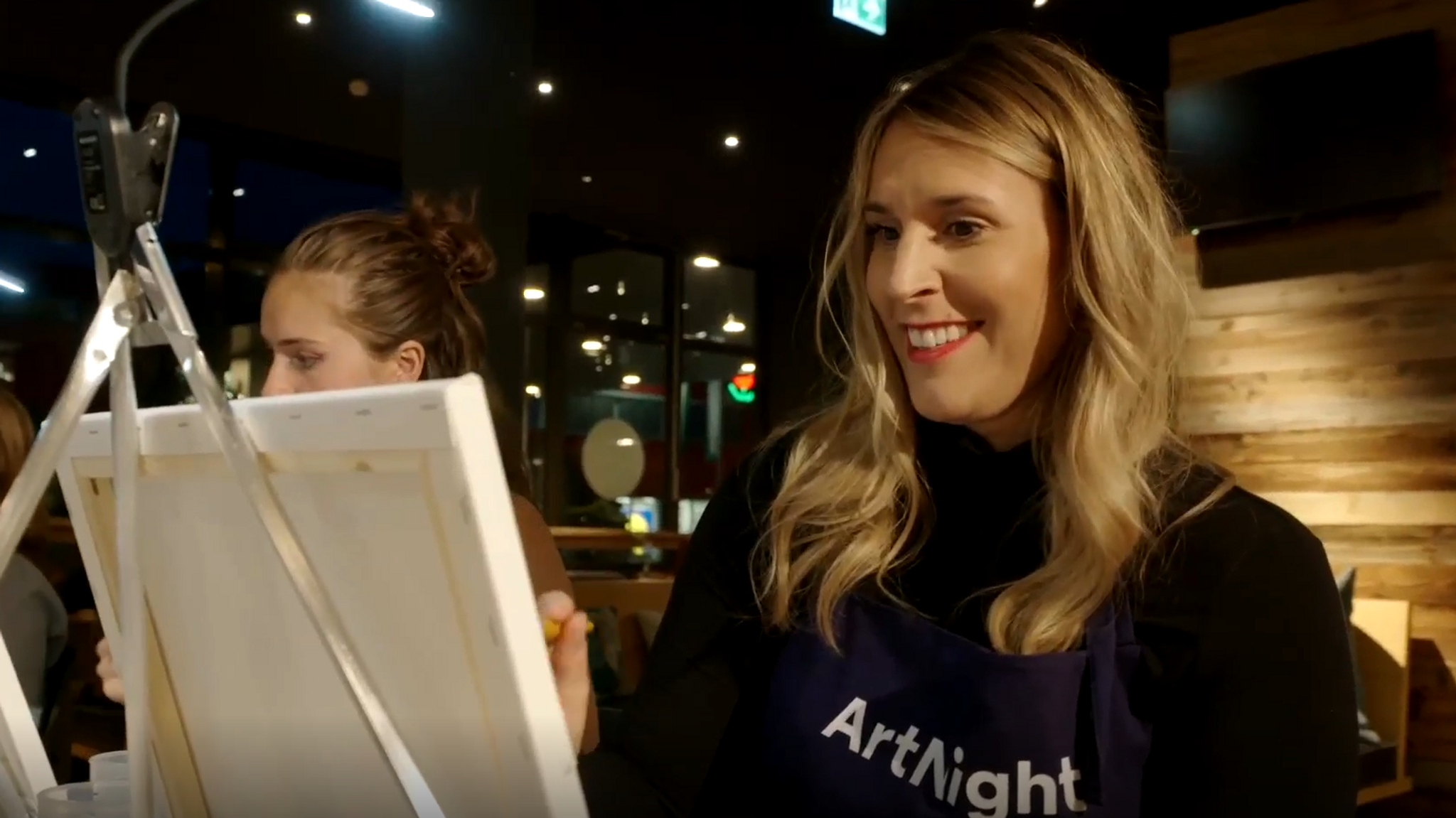 Gründerin Aimie-Sarah Carstensen sitzt in einem Café vor einer Staffelei und malt.