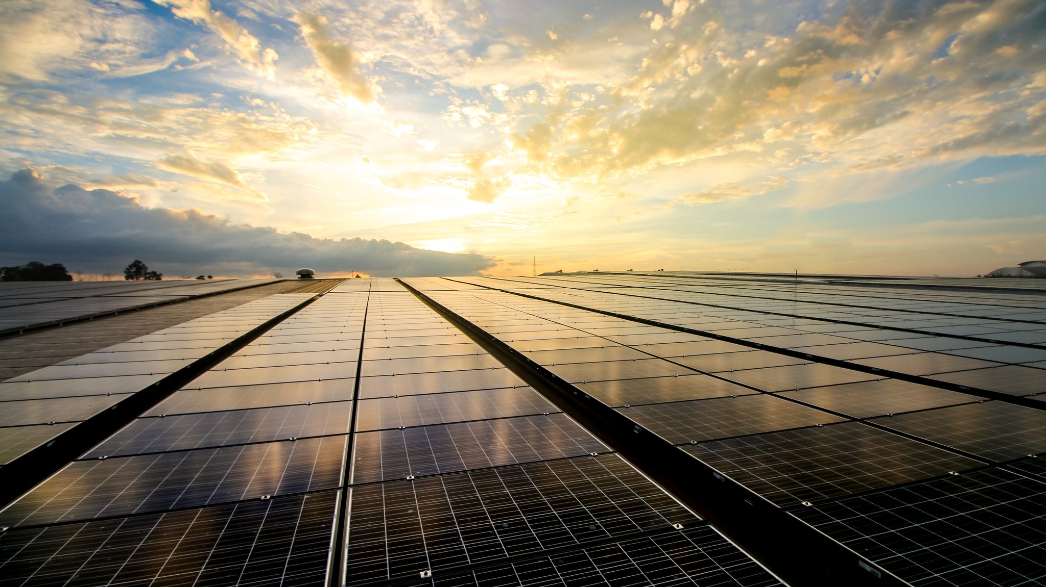 Eine Feld mit großen Solarpanels. Im Hintergrund strahlt die Sonne durch den bewölkten Himmel. (Symbolbild)