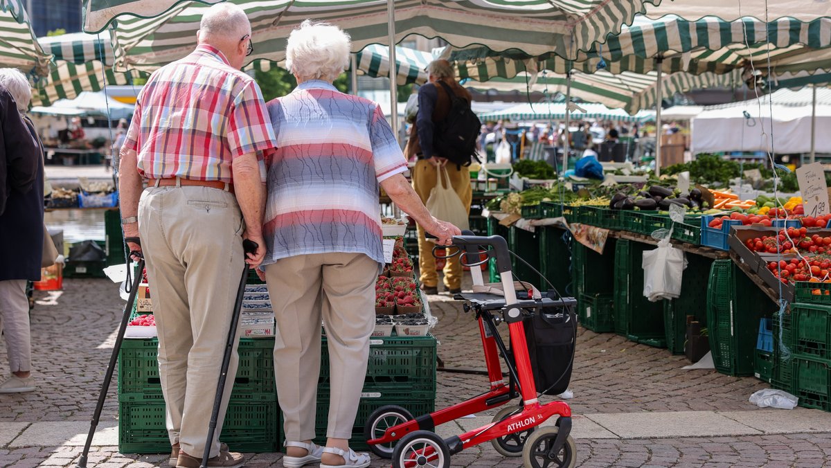 Zwei Senioren stehen an einem Stand eines Wochenmarkts. Eine gute Nahversorgung ist für ältere Menschen wichtig (Symbolbild).