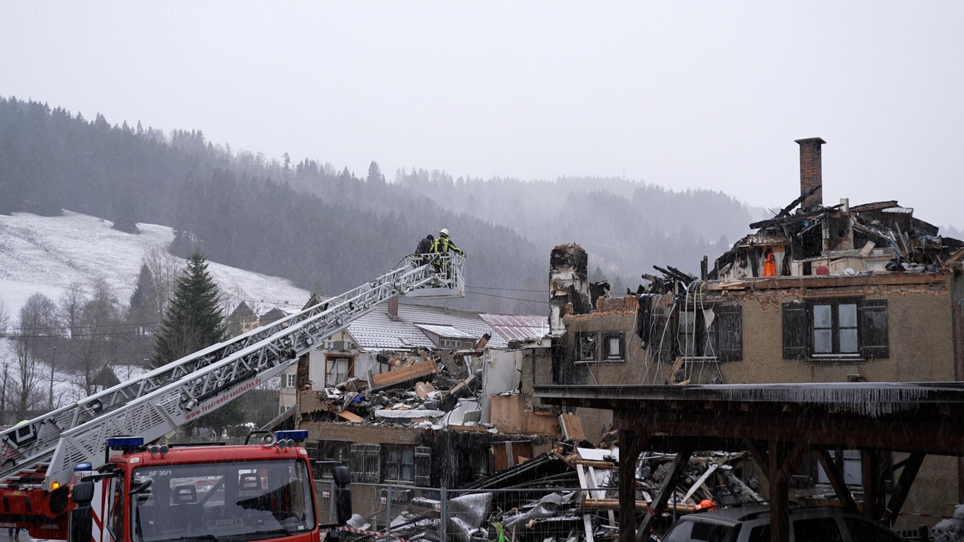 Feuerwehrleute auf einer Drehleiter neben einem völlig zerstörten Wohnhaus 