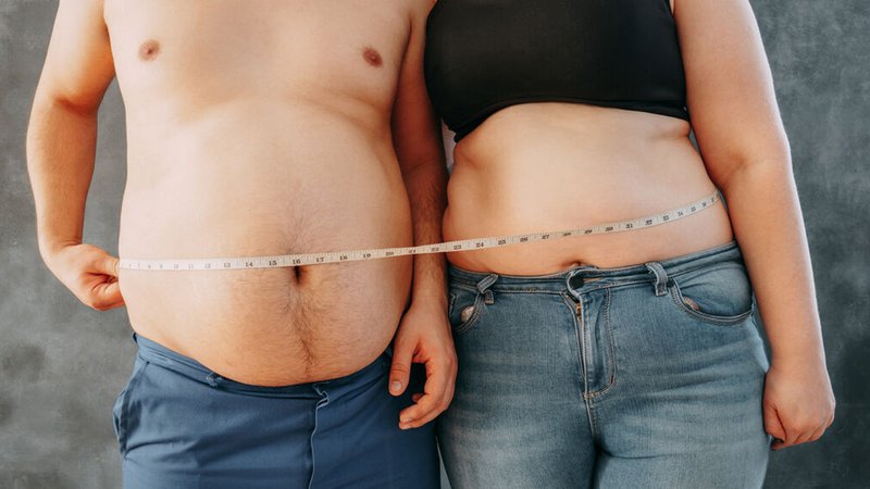 Frau und Mann stehen nebeneinander und halten ein Maßband um ihre Bäuche. | Bild: stock.adobe.com/Vadym Frau und Mann stehen nebeneinander und halten ein Maßband um ihre Bäuche.