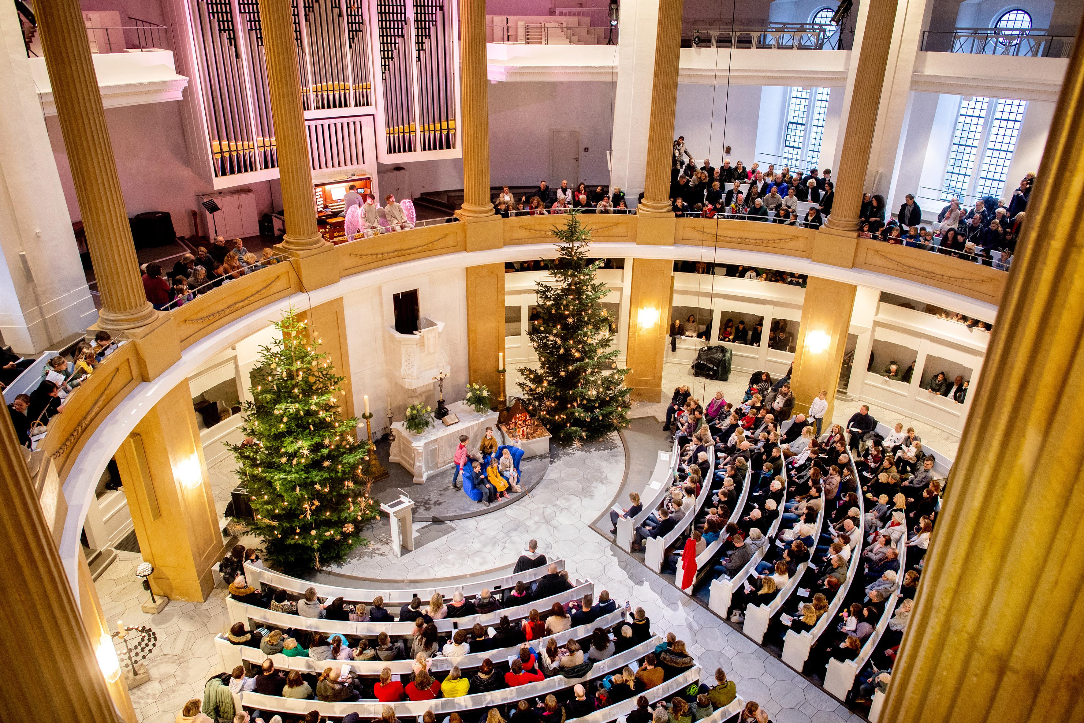 Eine volle Kirche mit Weihnachtsbäumen und Krippenspiel.