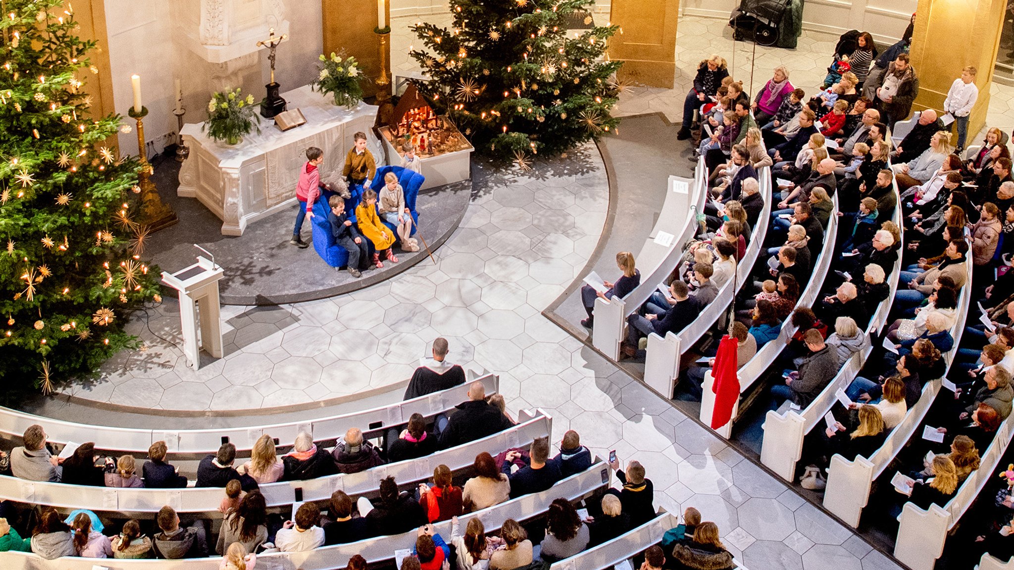 Eine volle Kirche mit Weihnachtsbäumen und Krippenspiel.