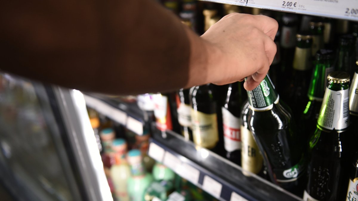 Ein Mann holt eine Flasche Bier aus einem Kühlschrank in einem Geschäft.