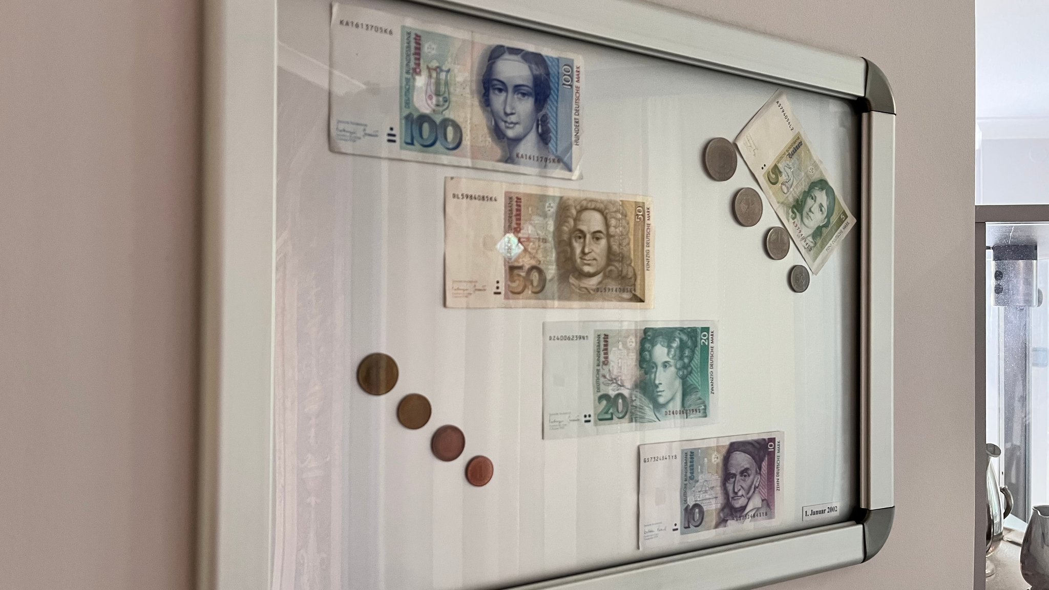 Jürgen R. aus München hat in seinem Hausgang einen Bilderrahmen mit alten Münzen und D-Mark-Scheinen.