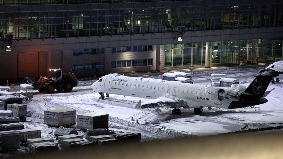 Eine Maschine der Lufthansa steht auf dem schneebedeckten Münchener Flughafen.