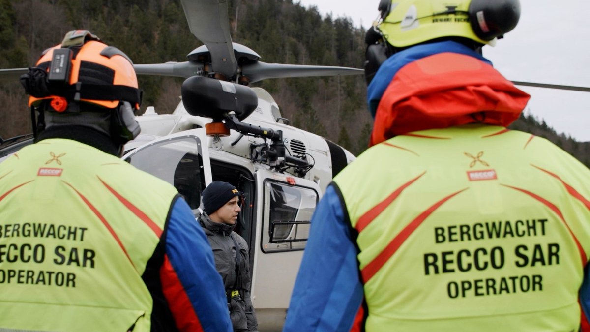 Zwei Einsatzkräfte mit Warnwesten stehen vor einem Polizeihubschrauber und sprechen mit dem Piloten.