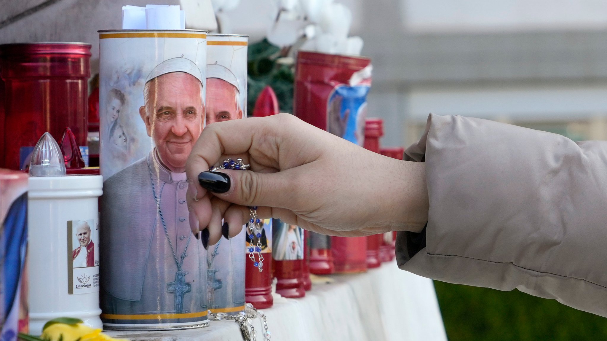 Eine Frau legt einen Rosenkranz neben Kerzen mit Bildern von Papst Franziskus vor der Poliklinik Agostino Gemelli nieder, wo der Pontifex wegen einer beidseitigen Lungenentzündung seit Freitag, 14. Februar stationär behandelt wird.