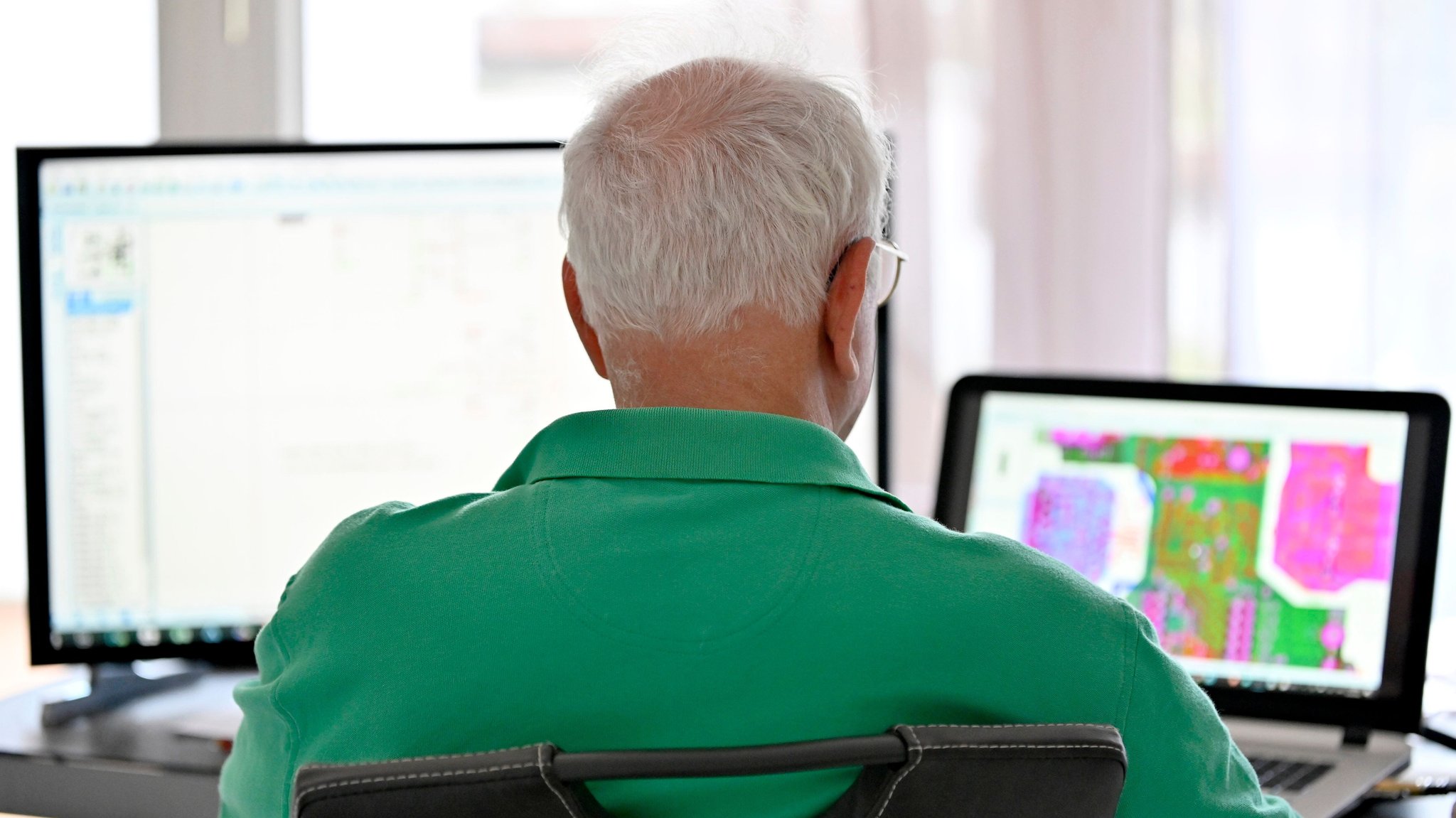 Ein Mann mit ergrautem Haar sitzt vor zwei Bildschirmen. 