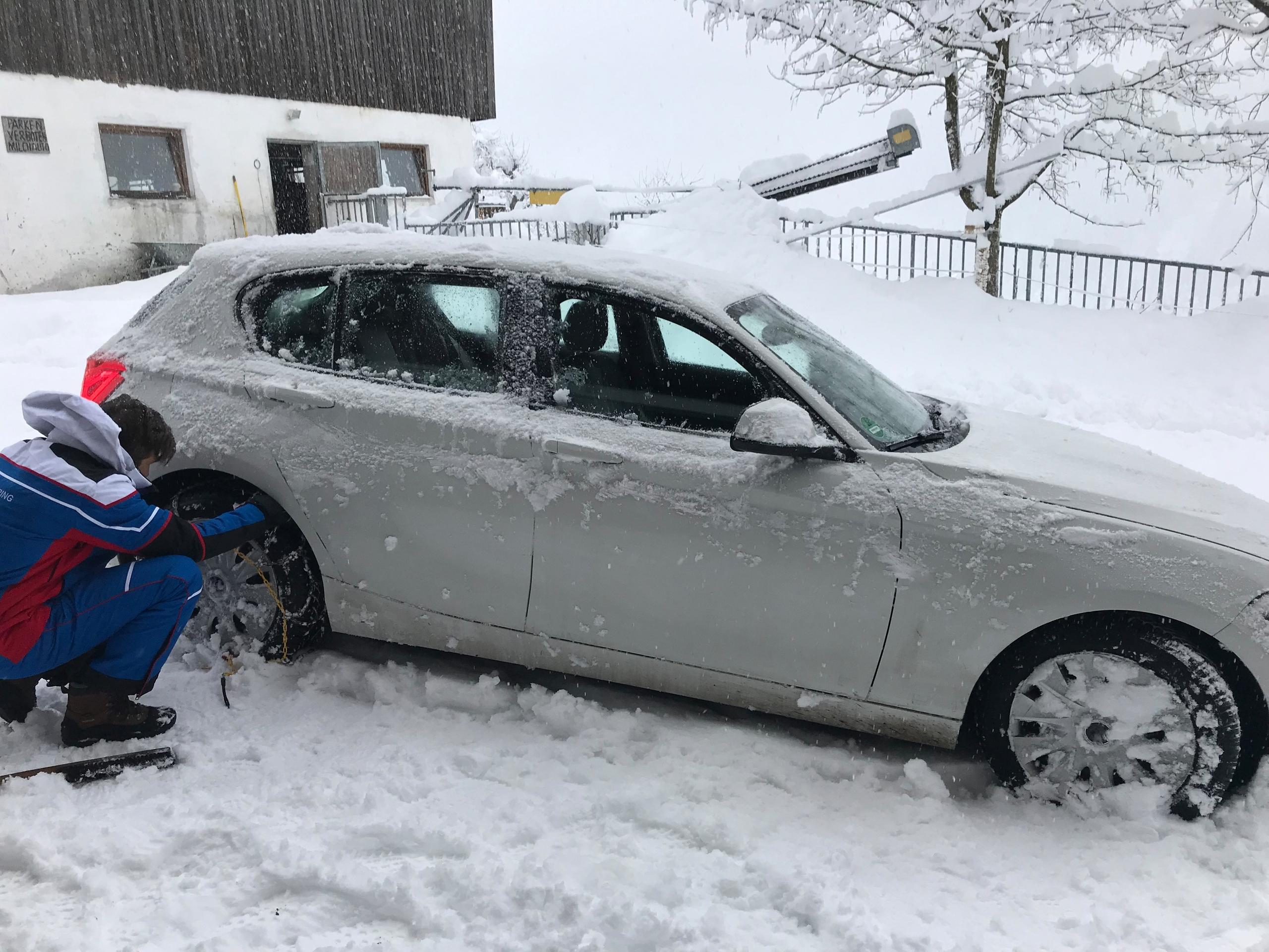 Ein Mann legt nach starkem Schneefall in den Alpen Schneeketten an einem Auto an.