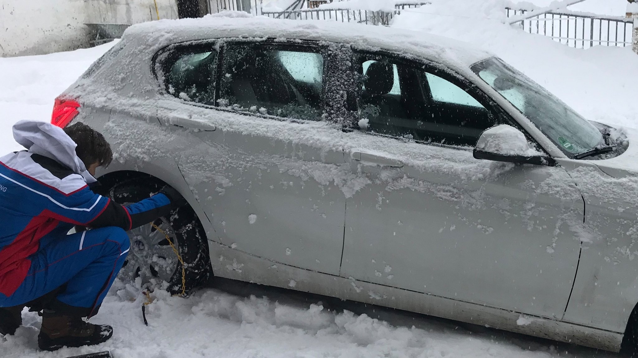 Ein Mann legt nach starkem Schneefall in den Alpen Schneeketten an einem Auto an.