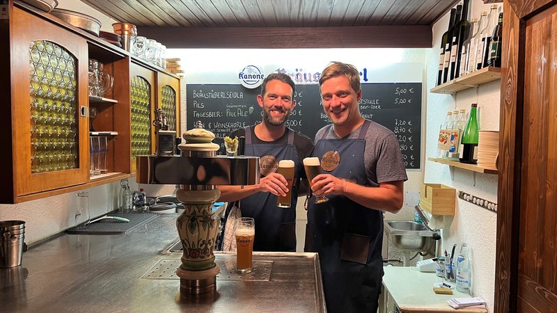 Zwei Männer stehen mit Bier in der Hand an einem Zapfhahn.