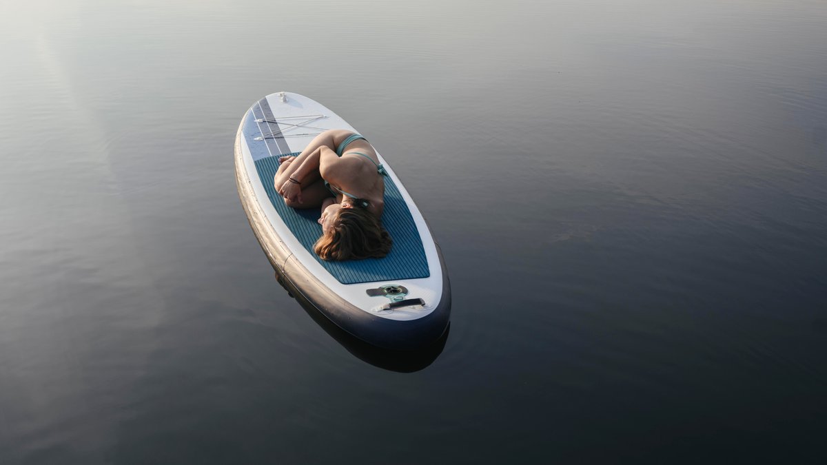 Frau liegt in Embryonalstellung auf einem SUP auf dem See