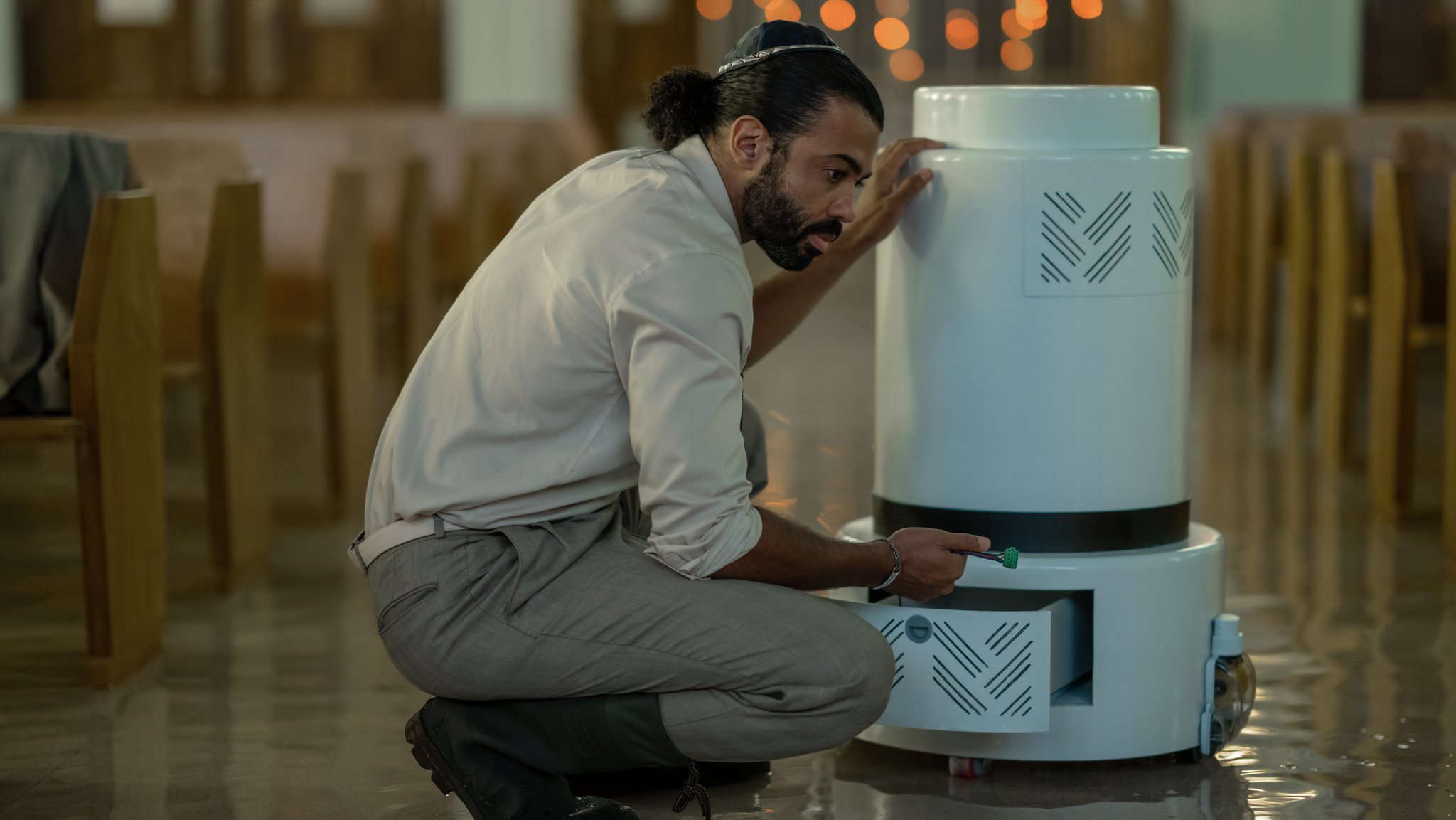 Daveed Diggs als Rabbiner kniet in einer Szene der Serie "Extrapolations" neben einem Saugroboter auf dem geflutetem Boden seiner Synagoge.