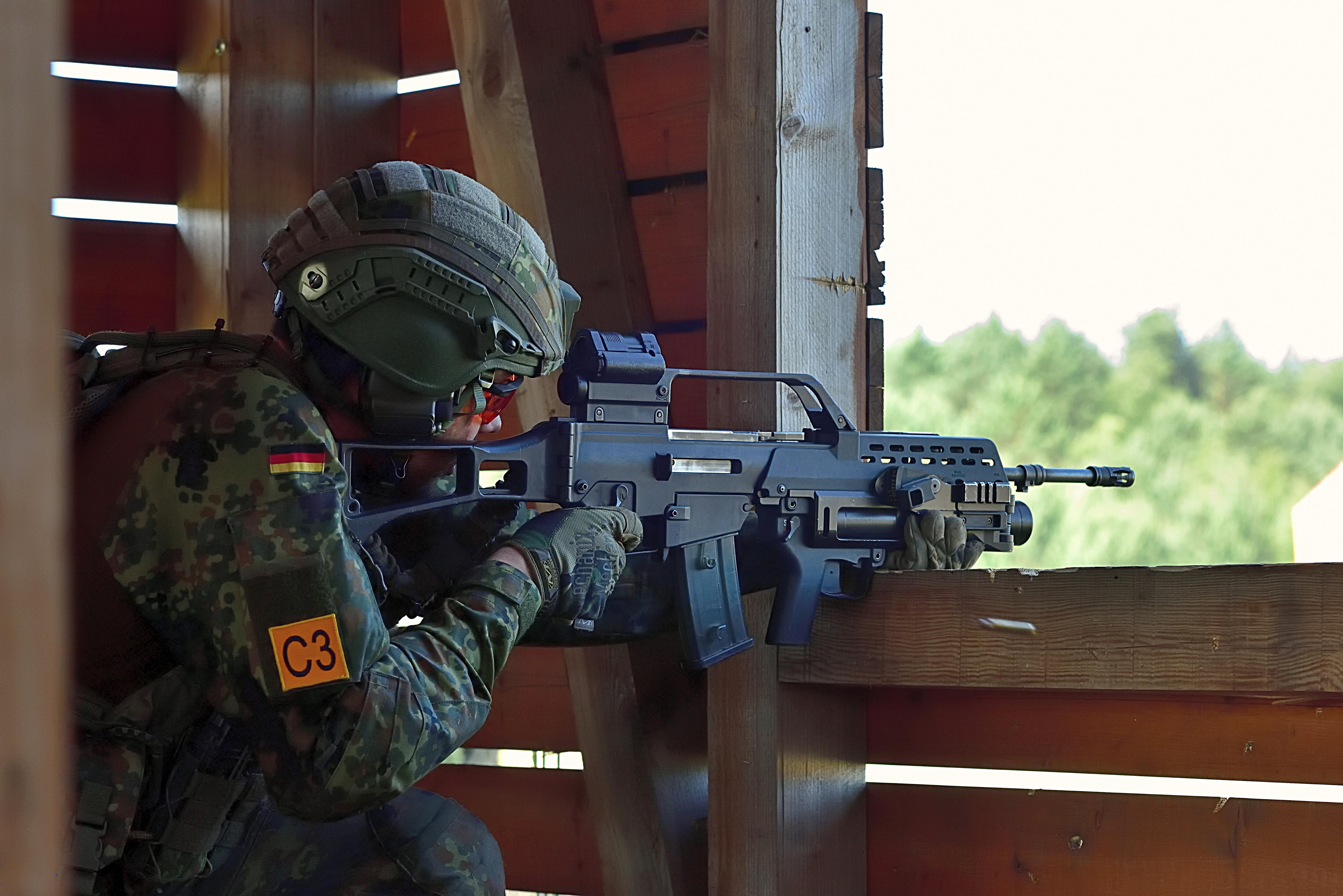 Ein Infanterie-Soldat der Bundeswehr sitzt während einer Gefechtsübung in einem Schießstand, hält eine Maschinenpistole im Anschlag und schaut durch das Zielfernrohr