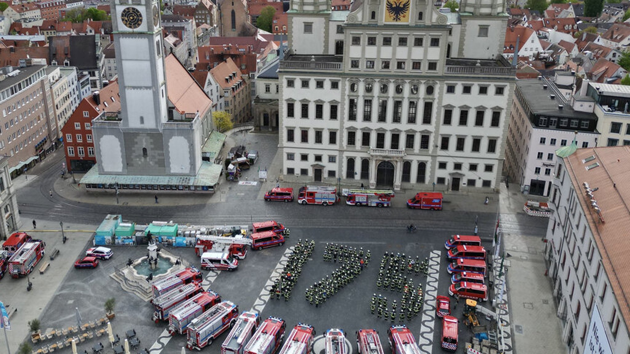 Vor dem Augsburger Rathaus haben sich Feuerwehrleute versammelt und bilden in Formation die Zahl "175". Um sie herum parken verschiedenste Feuerwehrfahrzeuge. Aufgenommen wurde das Foto anlässlich des 175-jährigen Jubiläums, das die Feuerwehr Augsburg am 14. und 15. September groß feiern wird.