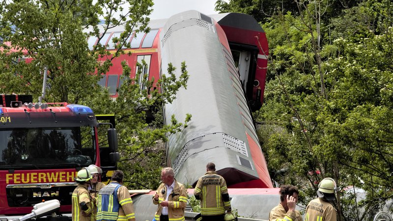 Ein entgleister Waggon eines Regionalzugs hängt an einer bewaldeten Böschung. Davor stehen Feuerwehrleute auf einer Straße neben einem Feuerwehrfahrzeug. | Bild: picture alliance/dpa/Garmisch-Partenkirchner Tagblatt/Josef Hornsteiner Ein entgleister Waggon eines Regionalzugs hängt an einer bewaldeten Böschung. Davor stehen Feuerwehrleute auf einer Straße neben einem Feuerwehrfahrzeug.