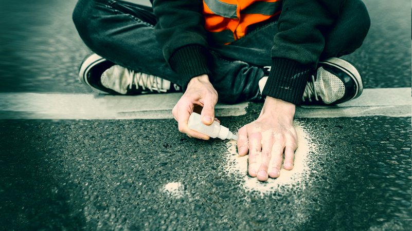 Ein Aktivist der Letzten Generation klebt sich die Hand mit Sekundenkleber auf der Straße fest.