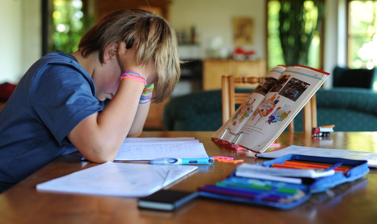 Ein Junge hält sich beim Erledigen seiner Hausaufgaben den Kopf. 