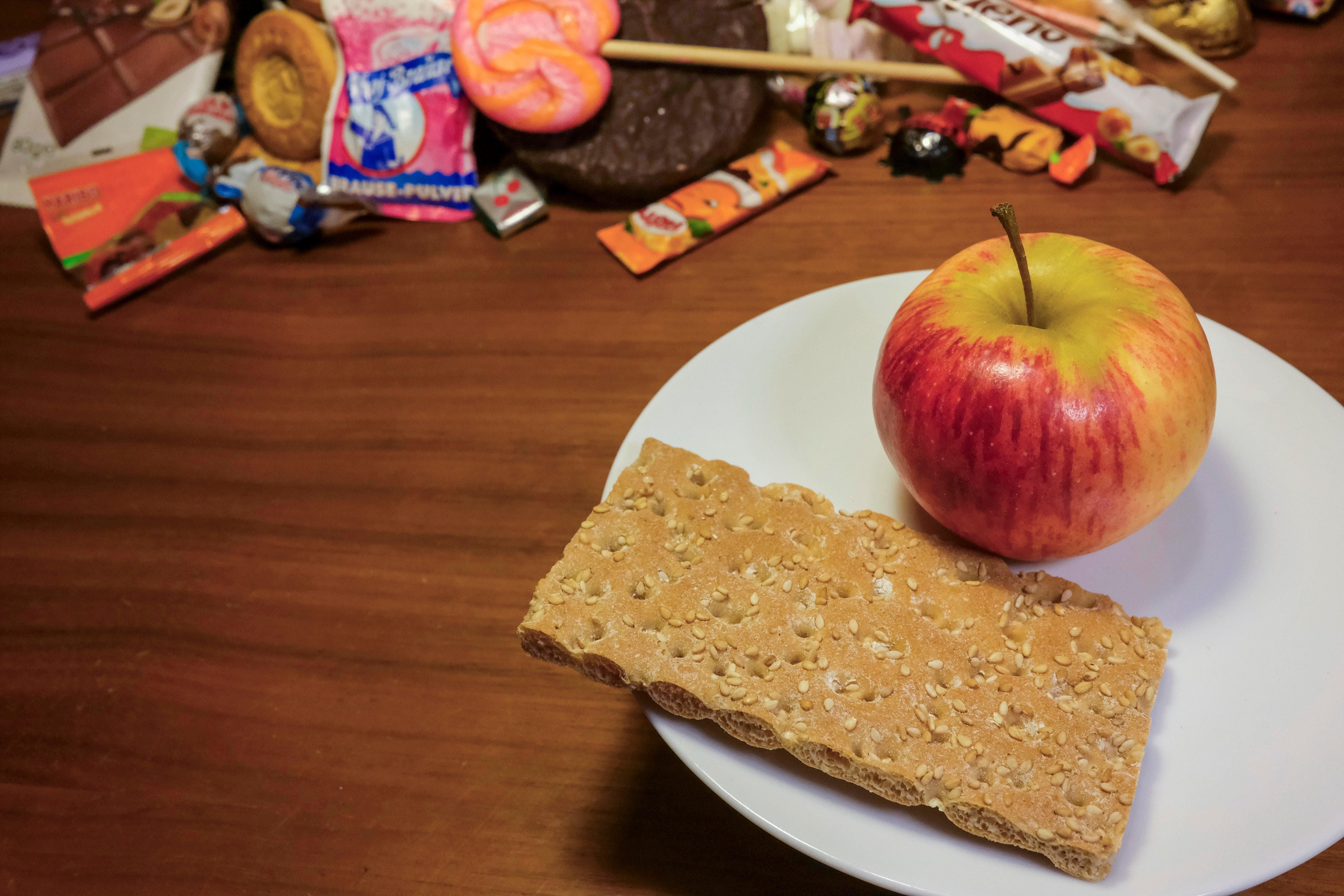 Apfel und Knäckebrot auf einem Teller neben Süßigkeiten.