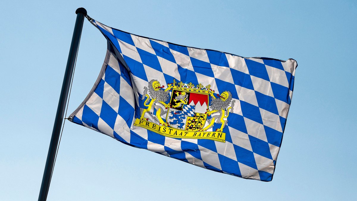 Ein blau-weiße Bayernfahne mit dem Wappen des Freistaats Bayern weht im Wind (Symbolbild).