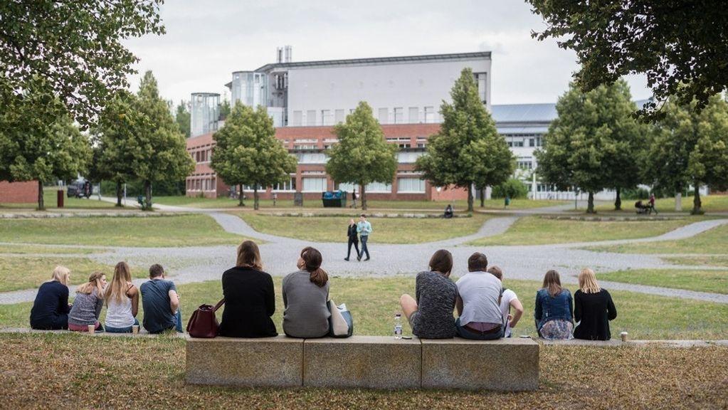 Mehrere Studierende der Universität Bayreuth sitzen am Rande des Campus. 