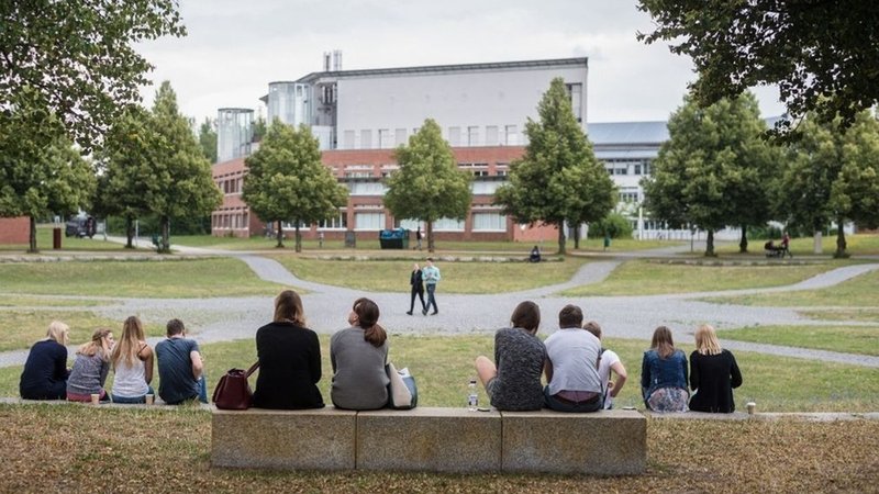 Mehrere Studierende der Universität Bayreuth sitzen am Rande des Campus. 