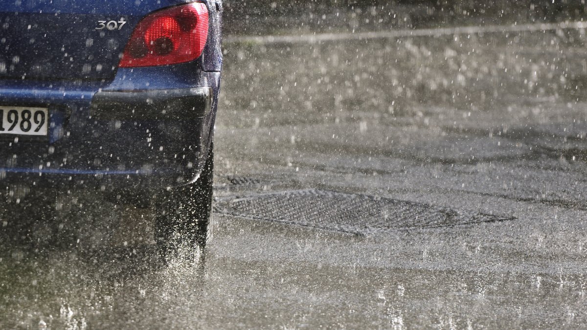 Ein Auto fährt bei Regen über eine nasse Straße.