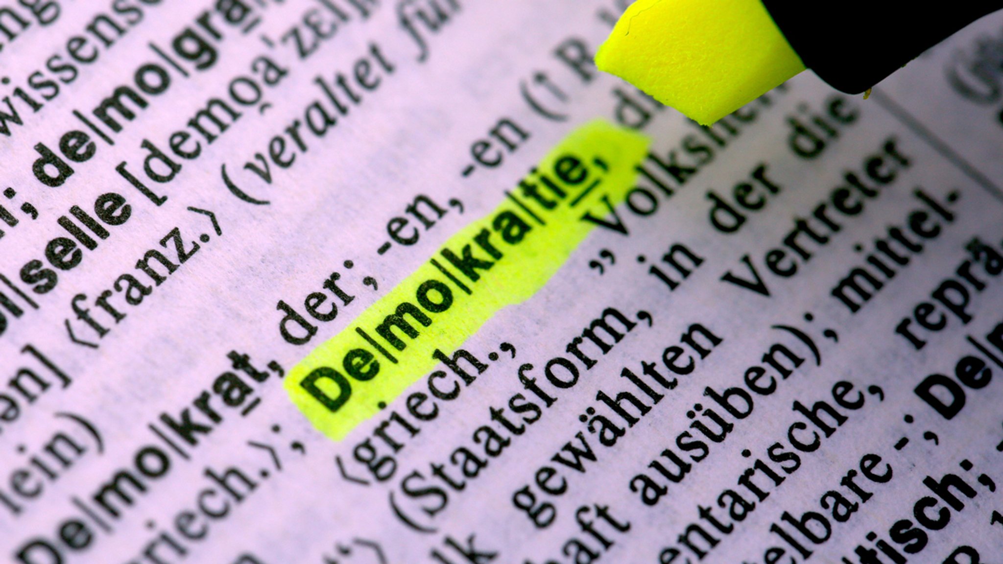 Ein Mann markiert im Duden das Wort "Demokratie". 