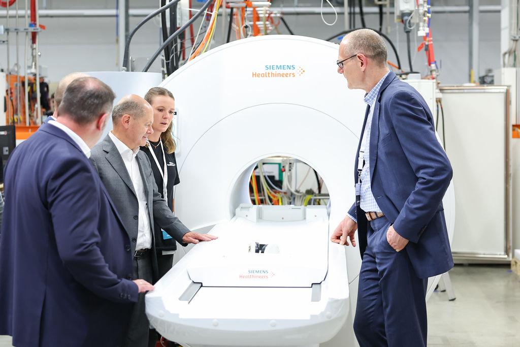 Bundeskanzler Olaf Scholz (2.v.l., SPD) steht während eines Besuchs der Siemens Healthineers AG in der Magnetresonanztomographie-Fertigung (MRT) an einem MRT in der Endprüfung.