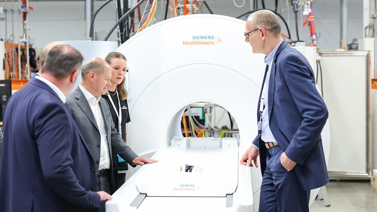 Bundeskanzler Olaf Scholz (2.v.l., SPD) steht während eines Besuchs der Siemens Healthineers AG in der Magnetresonanztomographie-Fertigung (MRT) an einem MRT in der Endprüfung.