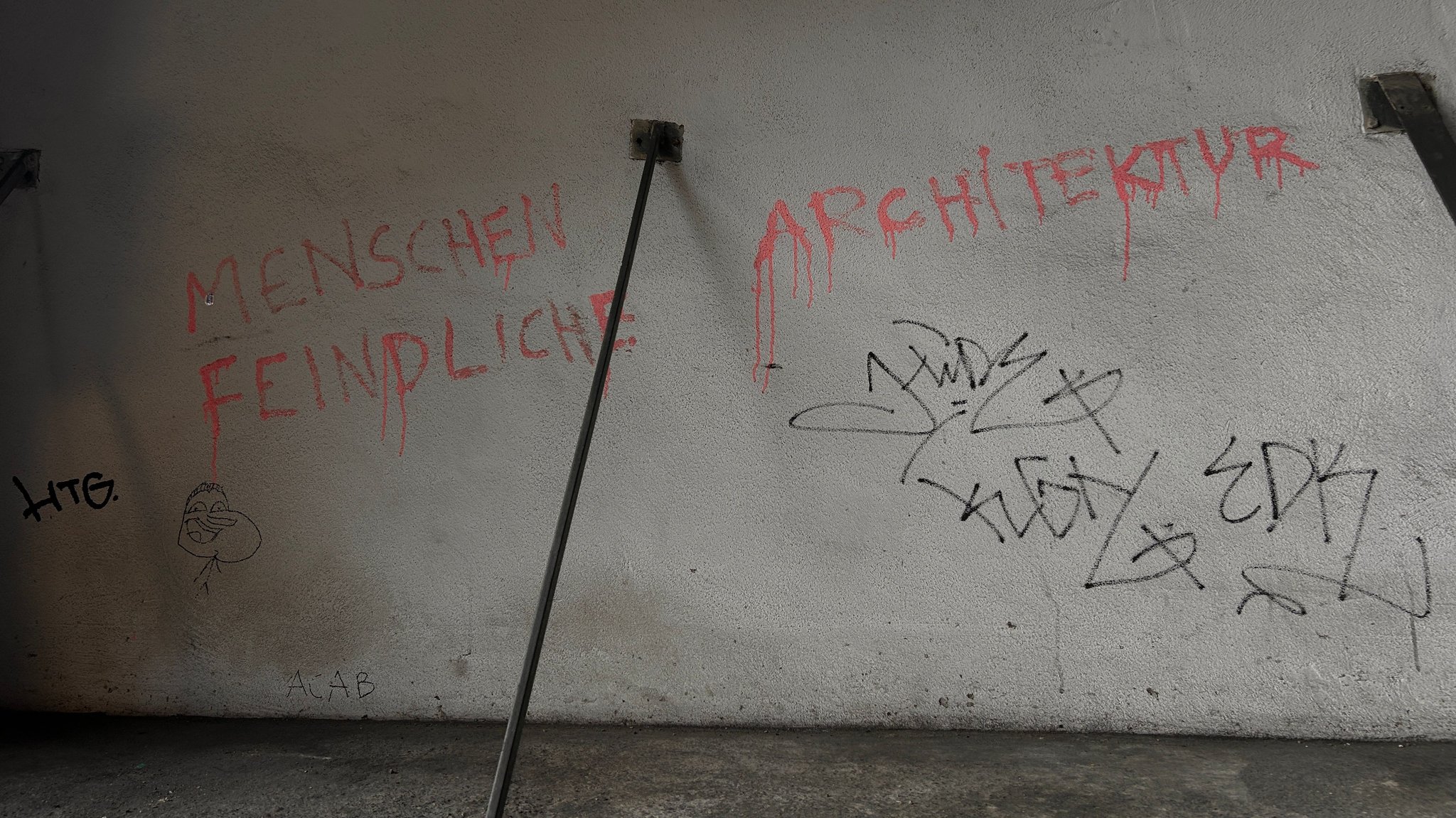Die Aufschrift "Menschenfeindliche Architektur" an einer Wand unter einer Unterführung in München.