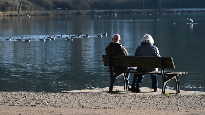 Zwei Senioren sitzen auf einer Bank und schauen auf einen See mit Gänsen. | Bild: picture alliance / SvenSimon | Malte Ossowski/SVEN SIMON Zwei Senioren sitzen auf einer Bank und schauen auf einen See mit Gänsen.