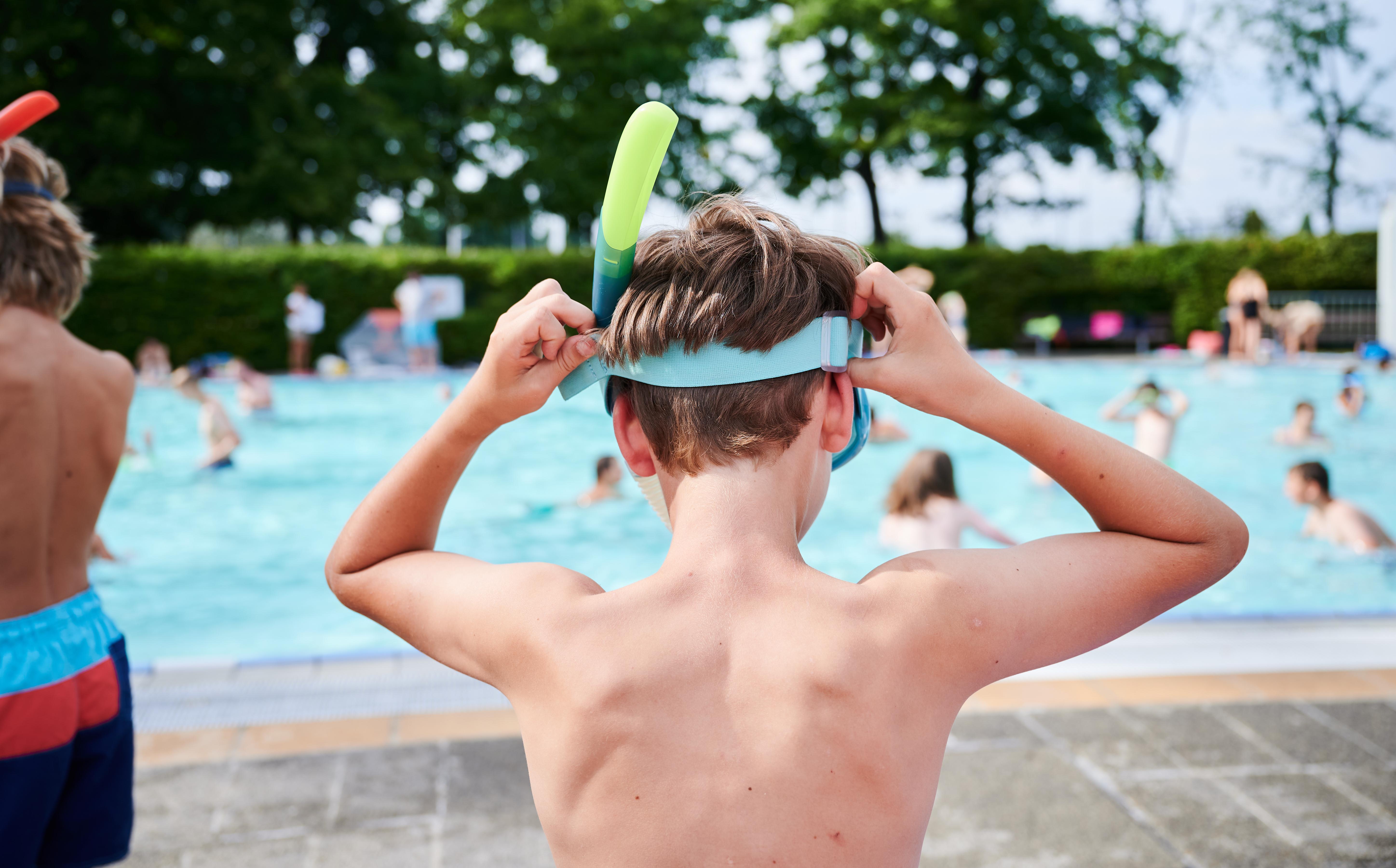Kind mit Taucherbrille vor einem Becken im Freibad