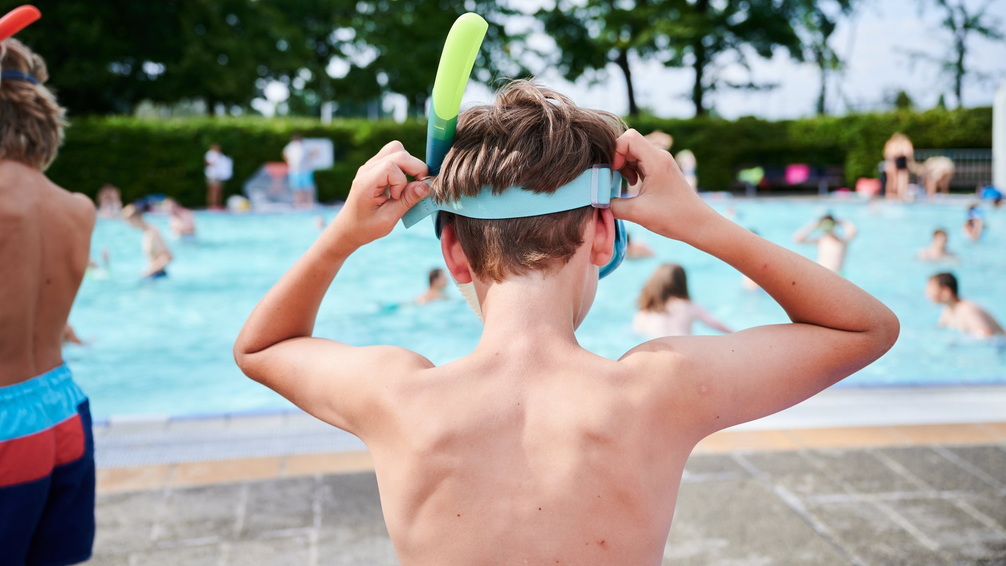 Kind mit Taucherbrille vor einem Becken im Freibad