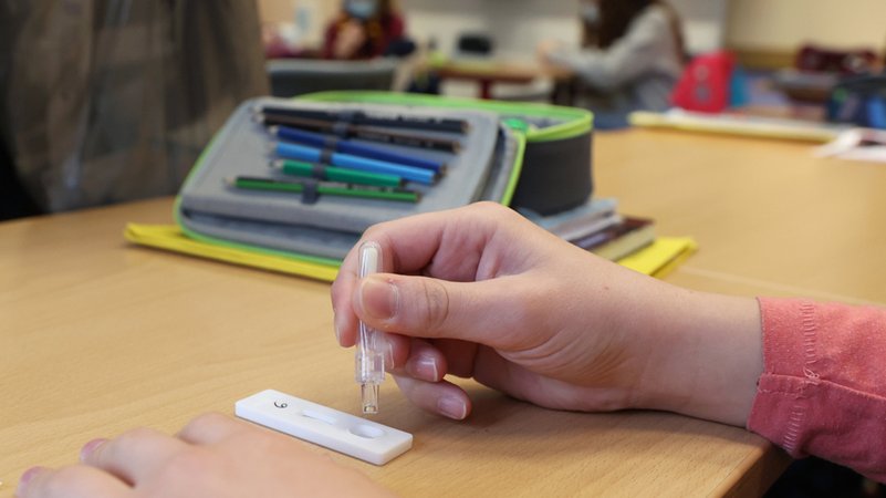 Eine Schülerin träufelt in einem Klassenraum eine Lösung nach einem selbst durchgeführten Corona-Test auf einen SARS-CoV-2-Antigentest.