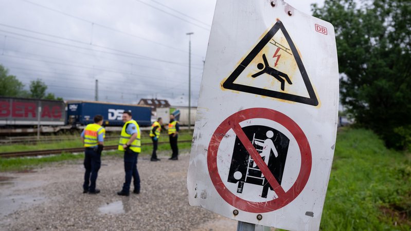Polizisten stehen am S-Bahnhof Trudering an einem Güterzug. Davor zwei Schilder, die vor der Gefahr eines Stromschlags warnen. hr
