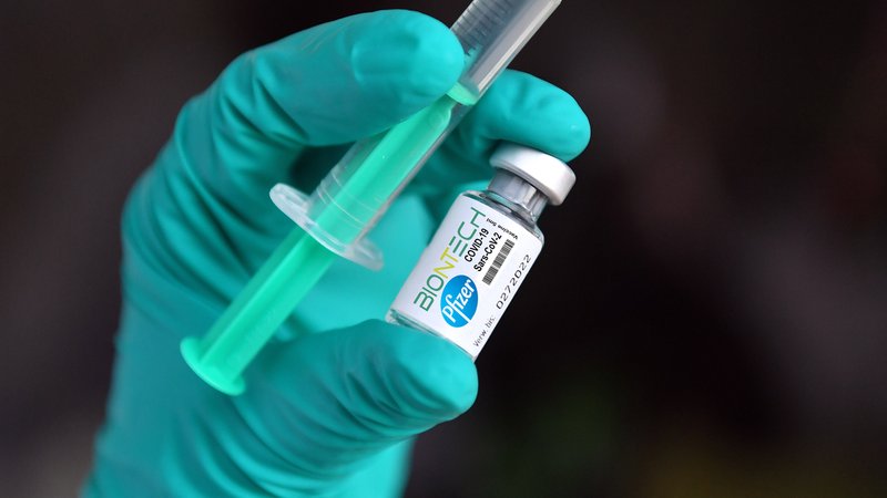 Hand in grünem Gummihandschuh hält Spritze und Impfstoff-Ampulle