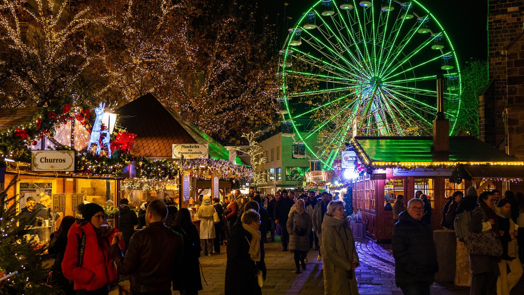 Weihnachtsmarkthütten für Essen und Trinken mit Menschen und Riesenrad, grün beleuchtet