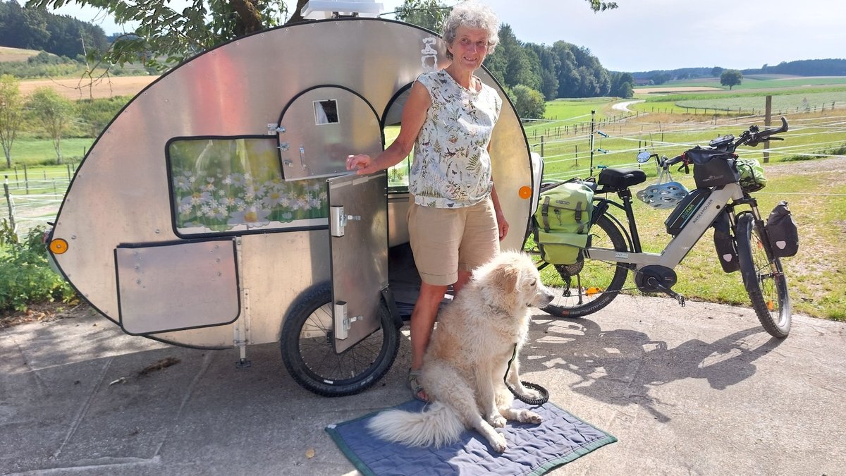 Susi Kronstein steht mit ihrem Hund Patchi vor ihrem Fahrrad-Wohnwagen.