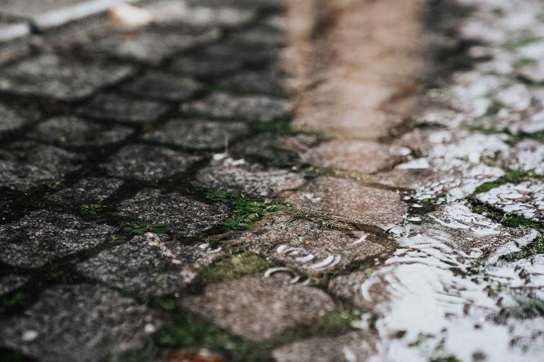 Regentropfen fallen in eine Regenpfütze auf Kopfsteinpflaster.